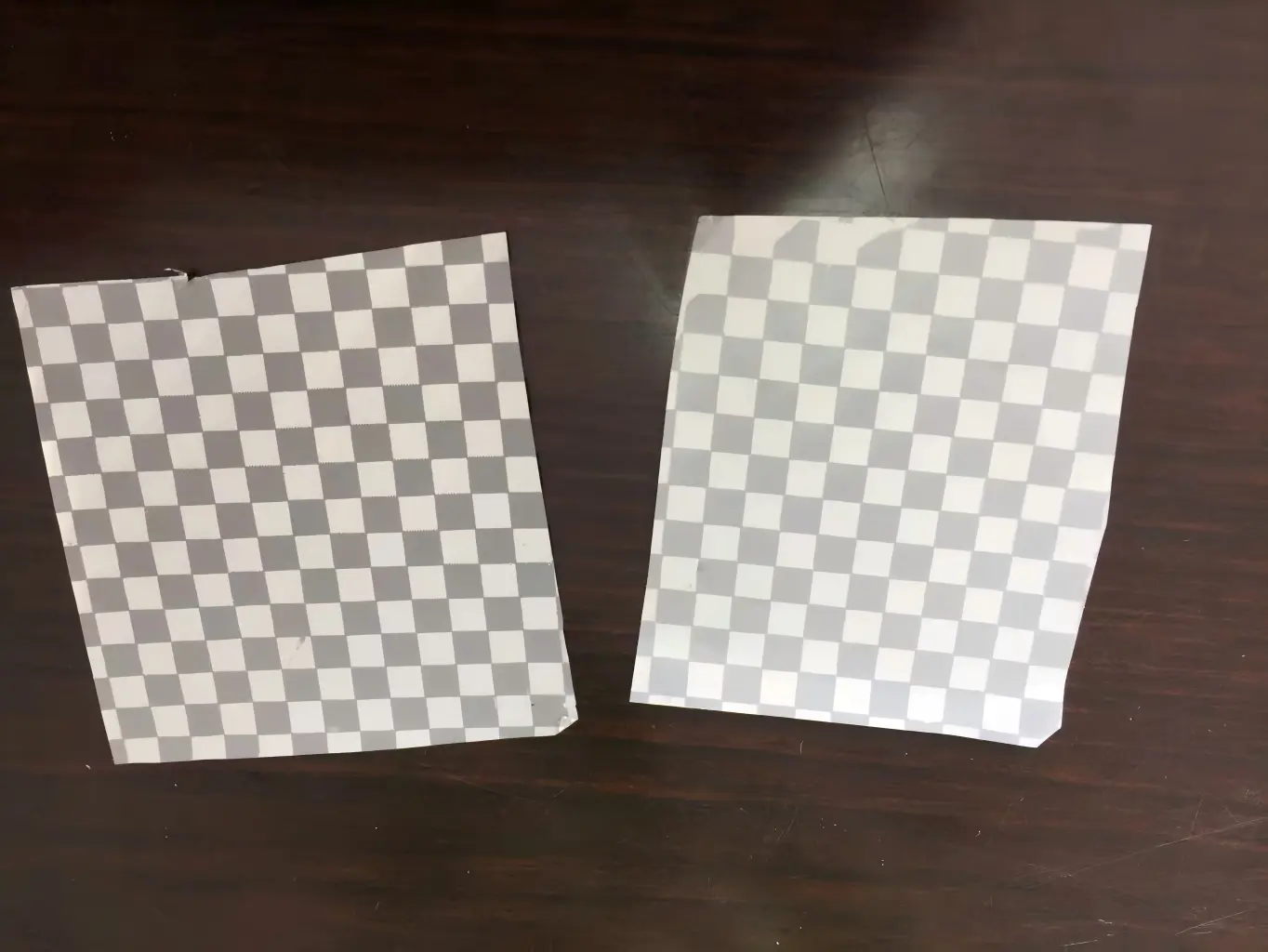 Early matte silver checkerboard tamper-evident material samples showing differences in surface tone and metallic appearance.